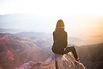 Photo: Woman sitting on rock atop mountain gazing out into distance