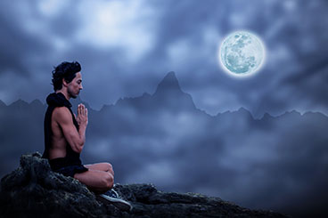 Photo: Man sitting meditating with moon in background